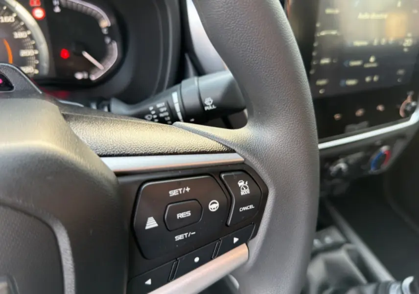 Gros plan sur le volant multifonctions du pick-up Isuzu D-MAX 2026, avec commandes de régulateur et écran tactile flou en arrière-plan.