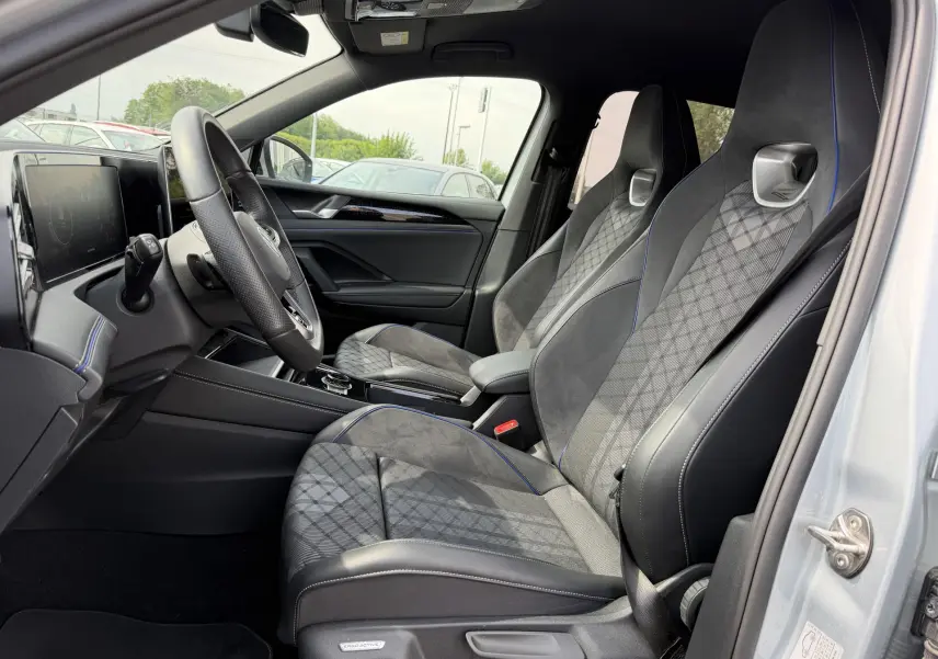 Vue intérieure côté conducteur du Volkswagen Tiguan 2025, sièges sport gris avec surpiqûres bleues et volant multifonction cuir.