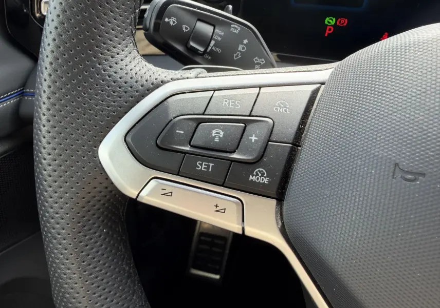 Gros plan sur les commandes multifonctions à gauche du volant cuir perforé du Volkswagen Tiguan 2025 gris.