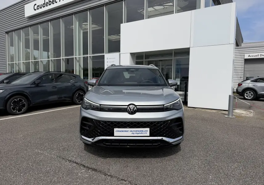 Volkswagen Tiguan gris vue de face, avec calandre noire et phares LED, devant un showroom automobile.