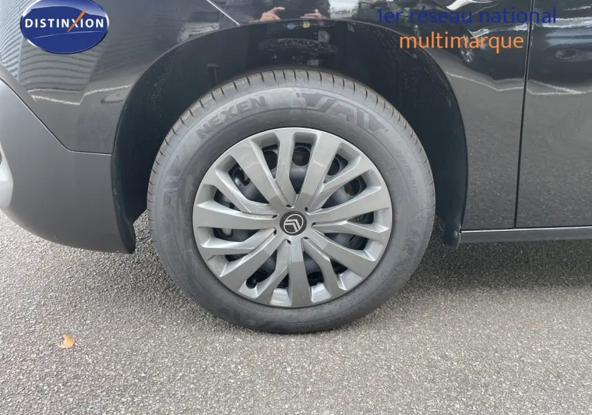 Gros plan sur la roue avant gauche d'un Citroën Berlingo noir Perla Nera métal avec jante argentée et logo Citroën.