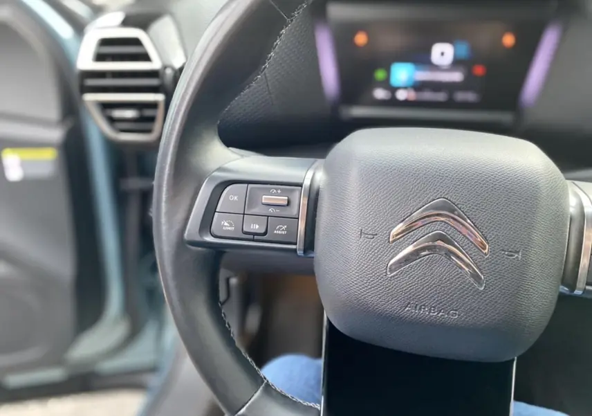 Gros plan sur le volant cuir noir de la Citroën C4 2021 avec commandes intégrées et logo chromé au centre.