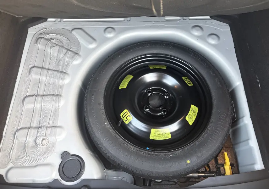 Vue plongeante sur la roue de secours noire dans le coffre d'une Citroën C4 II 2.0 HDI 150 HYB 2015.