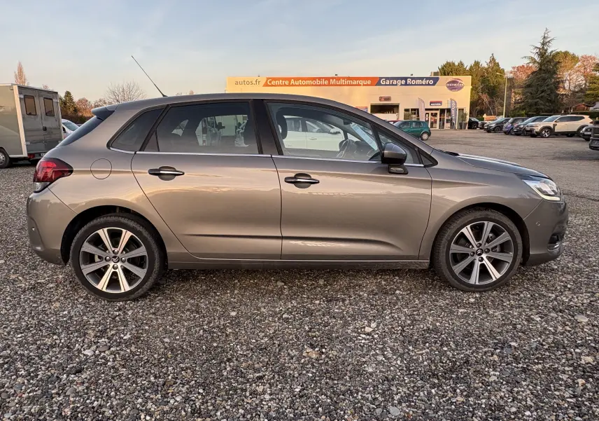 Profil côté gauche d'une Citroën C4 II gris métallisé de 2015 garée sur un sol gravillonné en extérieur.