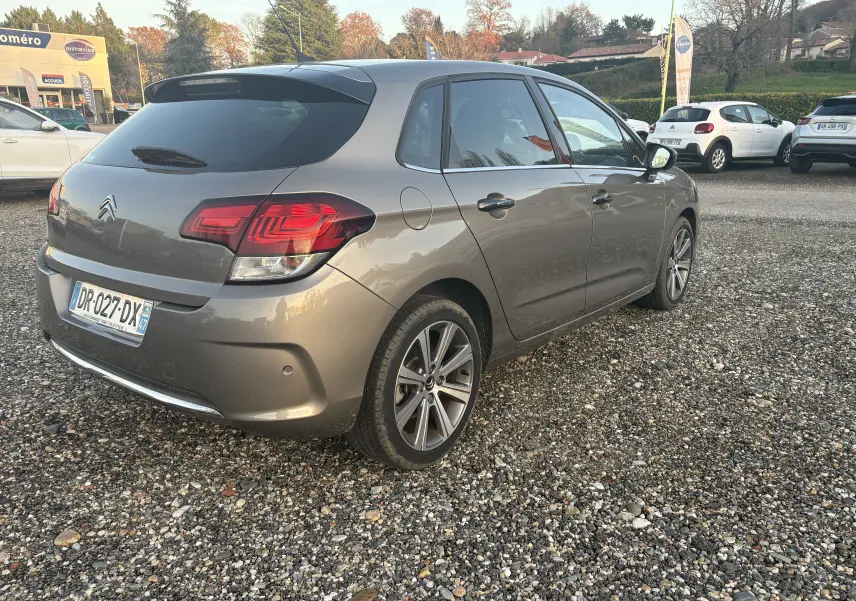 Citroën C4 gris métallisé vue 3/4 arrière droit sur parking gravillonné avec feux arrière LED distinctifs.