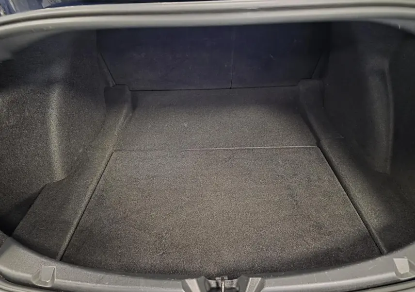 Coffre ouvert en vue plongeante d'une Tesla Model 3 RWD bleu foncé, montrant un espace de rangement vide et tapissé.
