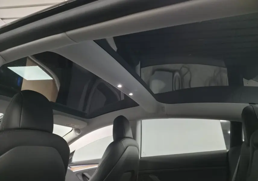 Vue intérieure arrière montrant le toit panoramique en verre et les sièges noirs d'une Tesla Model 3 RWD 2021.