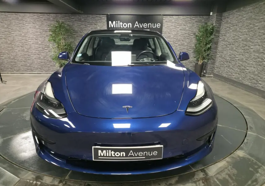 Vue frontale d'une Tesla Model 3 RWD bleu foncé avec phares LED et logo Tesla visible sur le capot.
