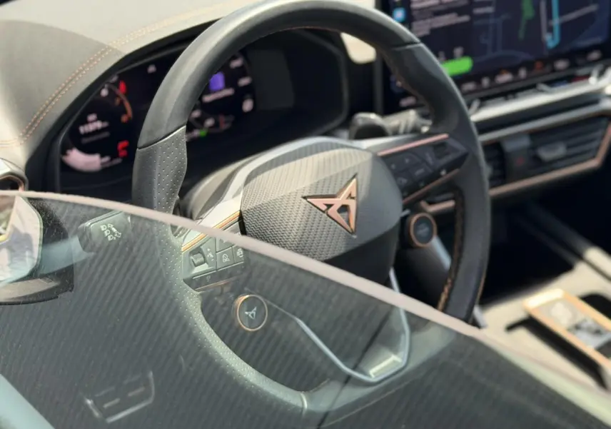 Gros plan sur le volant noir perforé avec logo CUPRA cuivré, tableau de bord numérique et écran tactile intérieur.