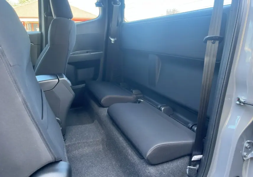 Vue intérieure côté droit du pick-up Isuzu D-MAX 2026 gris Kinabalu, montrant les sièges arrière rabattus et la ceinture de sécurité.