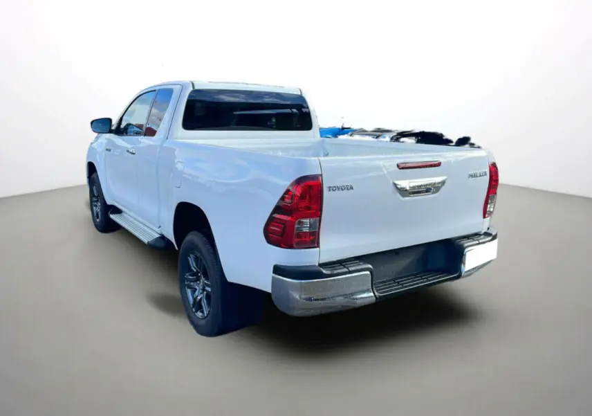 Toyota Hilux 4x4 blanc pur vu en 3/4 arrière droit, avec benne ouverte et feux arrière rouges distinctifs.