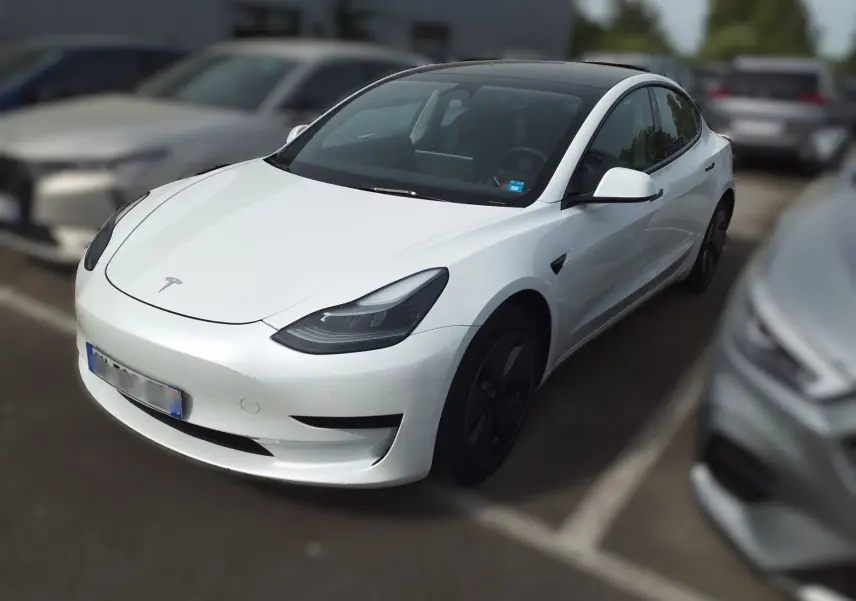 Tesla Model 3 blanc en 3/4 avant droit dans un showroom avec jantes noires et éclairage intérieur.