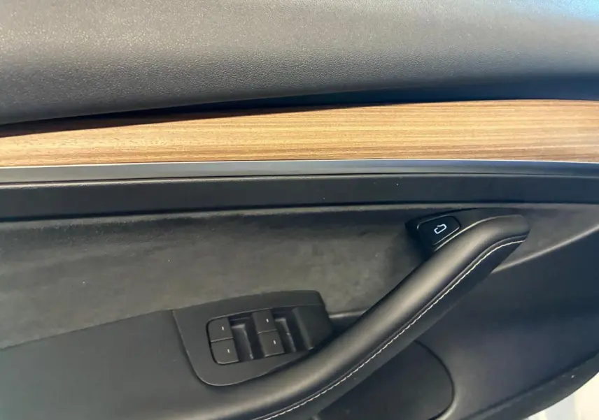 Détail de la porte intérieure côté conducteur d'une Tesla Model 3 blanche 2023, avec insert bois et commandes de vitres.
