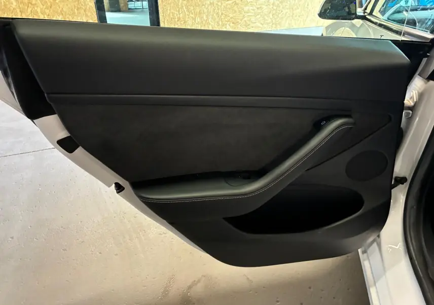 Vue intérieure de la porte avant gauche noire de la Tesla Model 3 blanche RWD 2023, avec poignée intégrée et finition épurée.