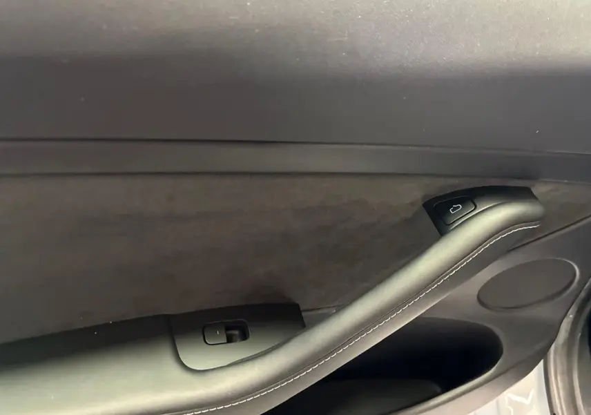 Détail de la poignée intérieure côté gauche de la porte d'une Tesla Model 3 blanche, avec bouton de verrouillage.