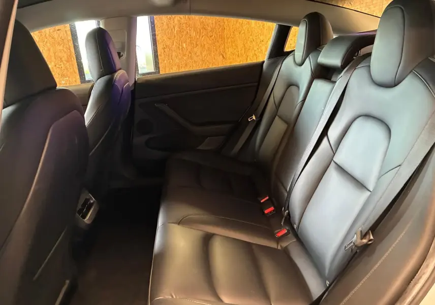 Vue intérieure arrière droite des sièges en cuir noir du Tesla Model 3 blanc 2023, version RWD Standard Plus.
