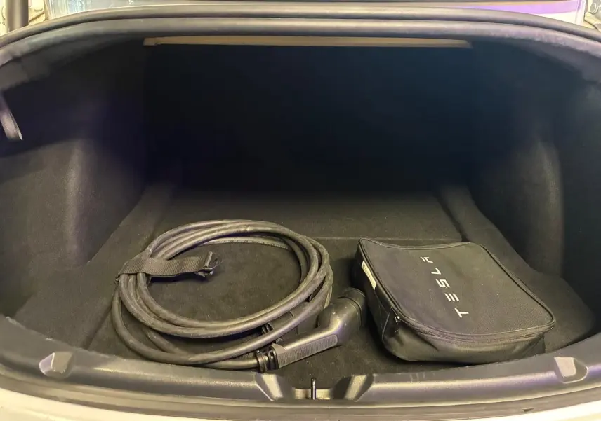 Coffre ouvert d'une Tesla Model 3 blanche 2023, vue de face, avec câble de recharge et sac de rangement Tesla.