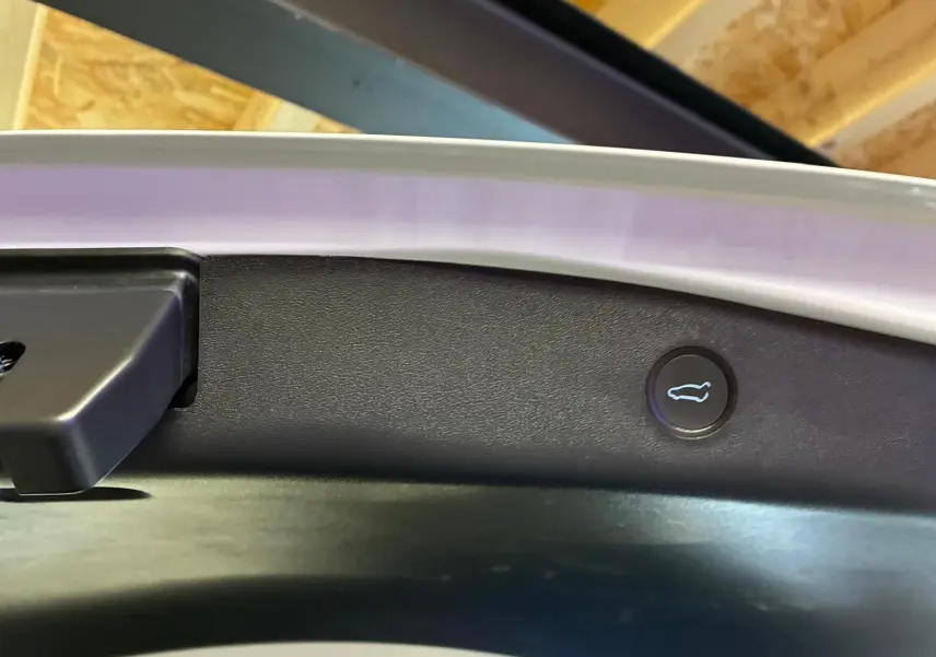 Gros plan sur le bouton d'ouverture du coffre arrière sur la partie intérieure d'une Tesla Model 3 blanche.