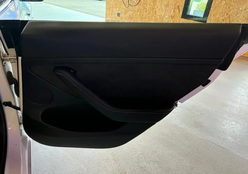 Vue intérieure de la porte côté gauche d’une Tesla Model 3 blanche, avec garniture noire minimaliste.