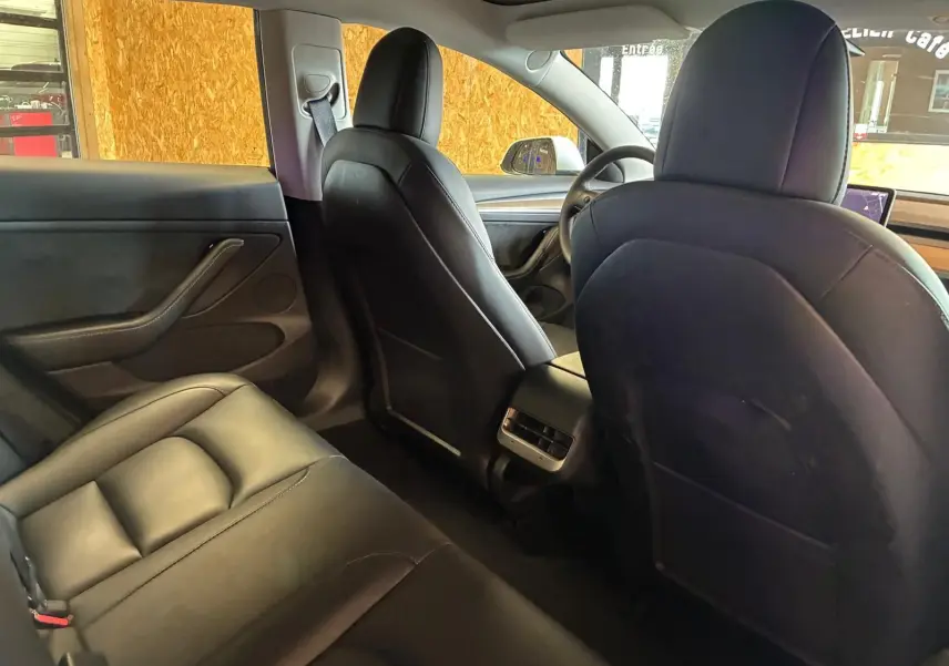 Vue intérieure arrière du Tesla Model 3 blanc 2023, montrant les sièges noirs en cuir et la console centrale avec aérateurs.