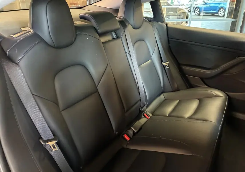 Vue intérieure des sièges arrière en cuir noir du Tesla Model 3 blanc, avec ceintures de sécurité visibles.