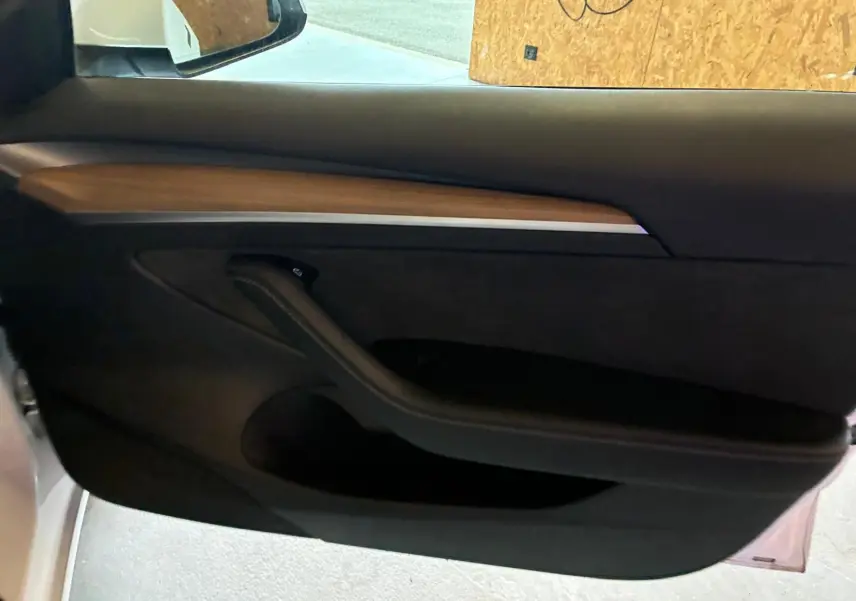 Intérieur de la porte côté conducteur d'une Tesla Model 3 blanche, avec insert en bois et poignée noire.