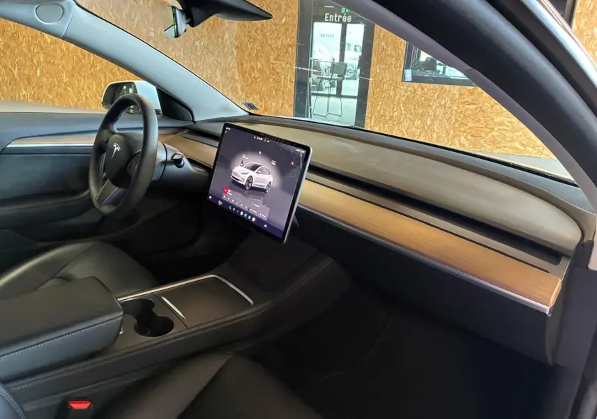 Intérieur de la Tesla Model 3 blanc, vue côté conducteur montrant le tableau de bord épuré avec écran tactile central.