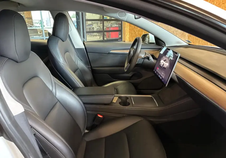 Vue intérieure côté gauche du Tesla Model 3 blanc 2023, mettant en valeur les sièges noirs et l'écran tactile central vertical.