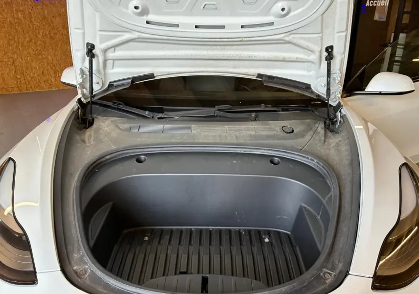 Vue avant rapprochée du coffre avant ouvert d’une Tesla Model 3 blanche, montrant l’espace de rangement électrique.