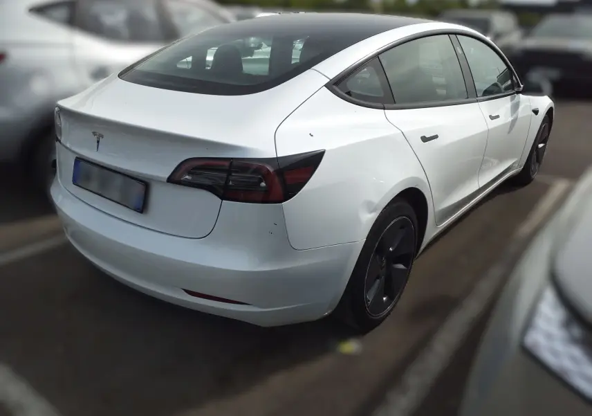 Tesla Model 3 blanc en vue 3/4 avant droit, avec jantes noires et éclairage intérieur bleu visible.