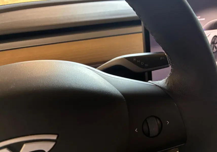 Gros plan sur le volant noir de la Tesla Model 3 blanc, version RWD 2023, avec levier de vitesses automatique visible.