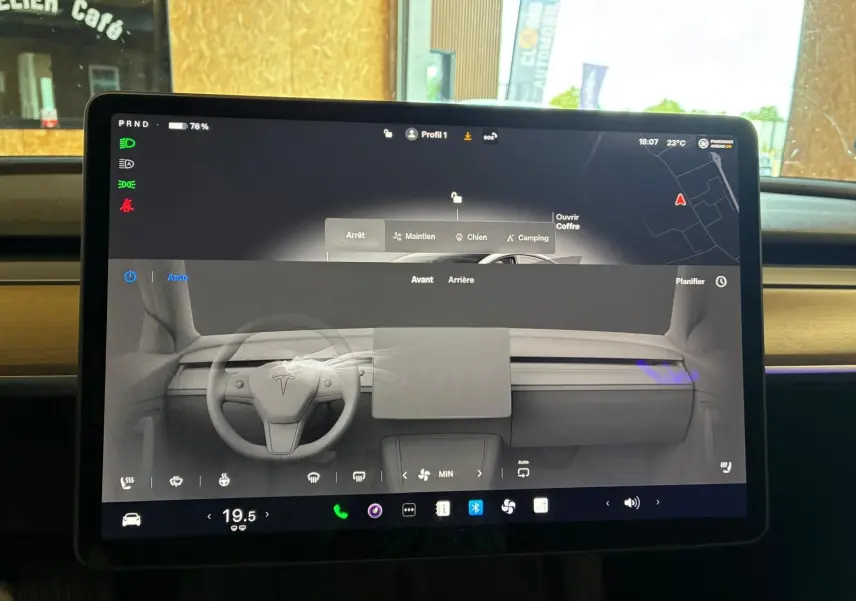 Écran central tactile affichant l'interface de contrôle du Tesla Model 3 blanc, vue intérieure frontale du tableau de bord.