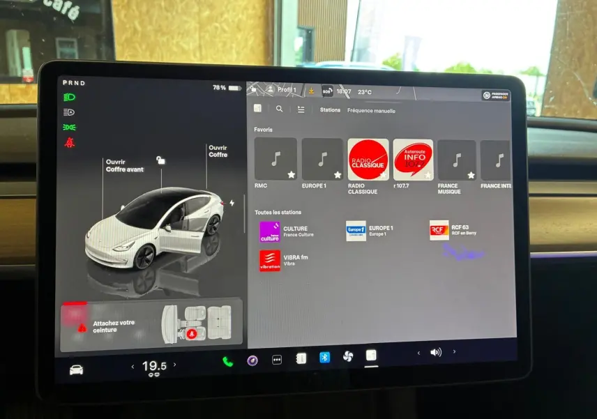 Écran tactile central de Tesla Model 3 blanc 2023 montrant l'interface multimédia et les options de coffre ouvert.