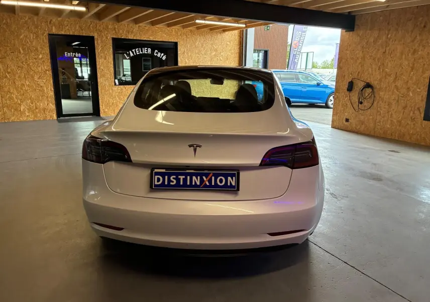 Vue arrière d'une Tesla Model 3 blanche RWD 2023, avec feux arrière teintés et plaque d'immatriculation Distinxion.