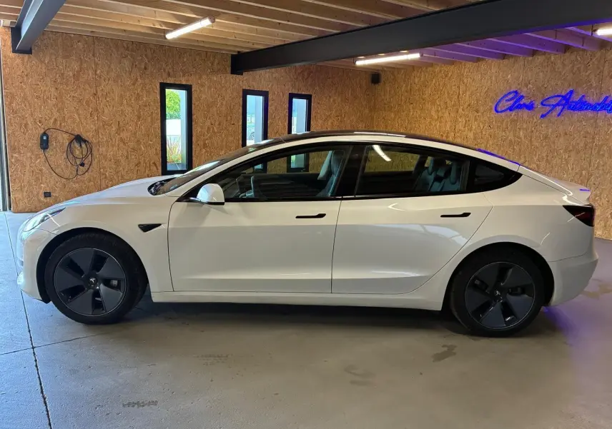 Vue de profil côté gauche d'une Tesla Model 3 blanche 2023, avec jantes noires et poignées affleurantes.