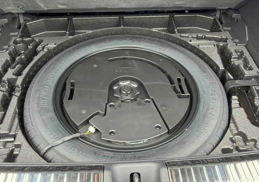 Vue plongeante sur la roue de secours compacte noire dans le coffre de l'Audi Q3 Sportback gris 2026.