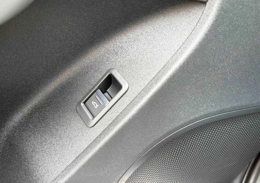 Détail du bouton d'ouverture électrique du hayon sur la garniture intérieure noire du coffre de l'Audi Q3 Sportback gris.