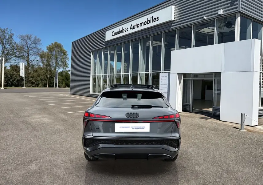 Vue arrière d'un Audi Q3 Sportback gris avec feux LED distinctifs, garé devant un bâtiment moderne.