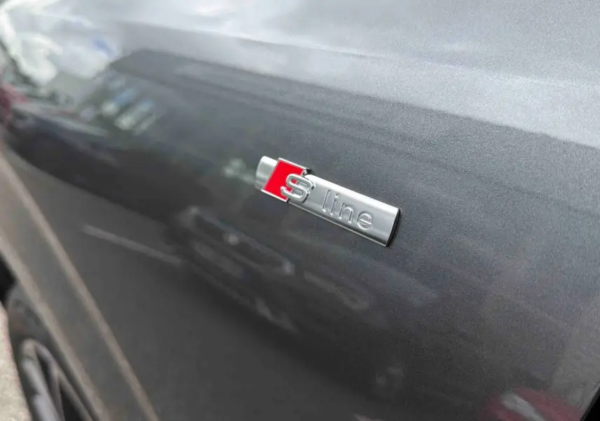 Gros plan sur l'emblème S line sur la porte côté gauche d'un Audi Q3 Sportback gris métallisé.