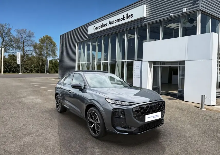 Audi Q3 Sportback gris, vue 3/4 avant droit, avec jantes noires et calandre noire brillante devant un showroom.