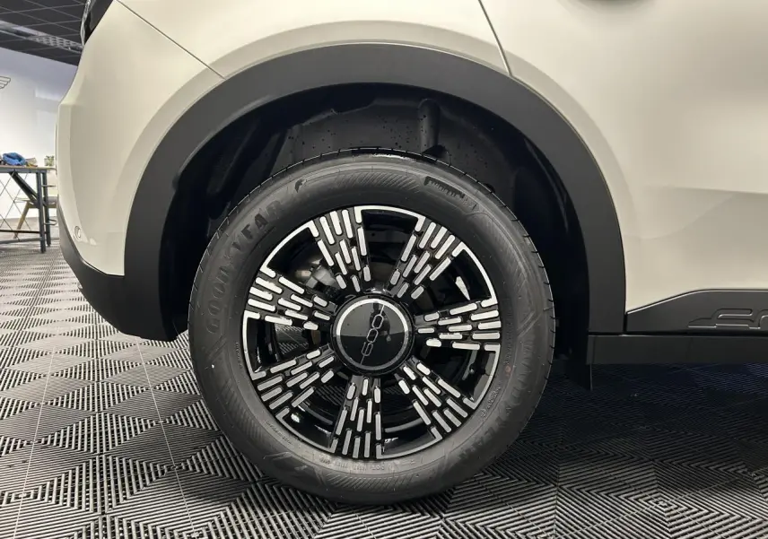 Gros plan sur la roue arrière droite noire et blanche du FIAT 600 blanc, avec jante alliage au design moderne.