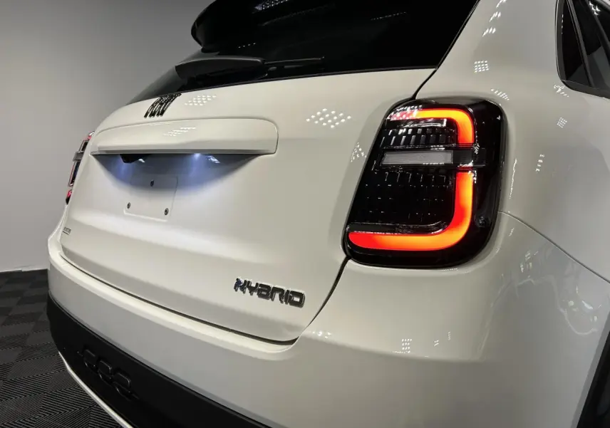 Vue arrière droite d'une FIAT 600 blanche hybride avec feux arrière LED allumés et logo Hybrid sur le hayon.