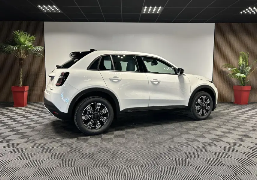 Vue latérale droite d'un FIAT 600 blanc avec jantes alliage noires et toit noir dans un showroom.