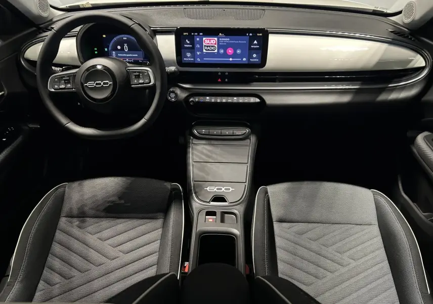 Vue intérieure frontale du tableau de bord et des sièges gris bicolores du Fiat 600 hybride avec écran tactile et volant multifonctions.
