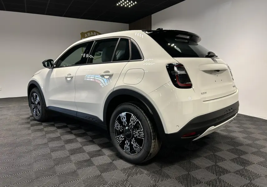 Vue 3/4 arrière droite d'un FIAT 600 blanc avec jantes noires et toit noir brillant dans un showroom.