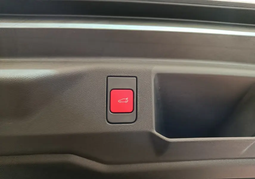 Bouton rouge d'ouverture électrique du coffre sur la garniture intérieure noire d'un Peugeot 5008 gris clair.