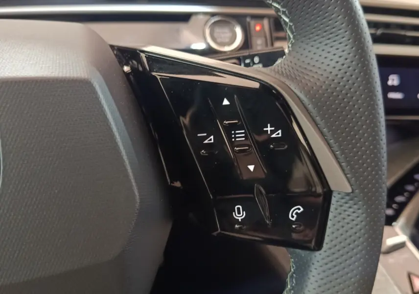 Gros plan sur les commandes noires au volant cuir perforé du Peugeot 5008 1.6 PHEV gris clair, intérieur moderne.