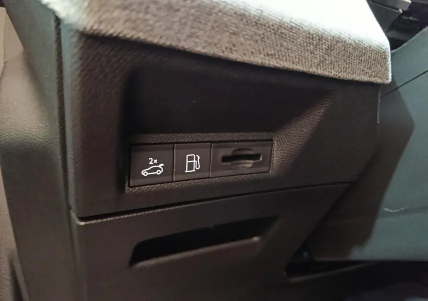Gros plan sur les commandes d'ouverture du coffre et du bouchon de carburant dans l'habitacle du Peugeot 5008 gris clair.