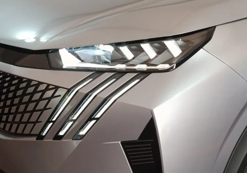 Gros plan sur l'avant droit gris clair du Peugeot 5008 2026, mettant en valeur ses phares LED et sa calandre distinctive.