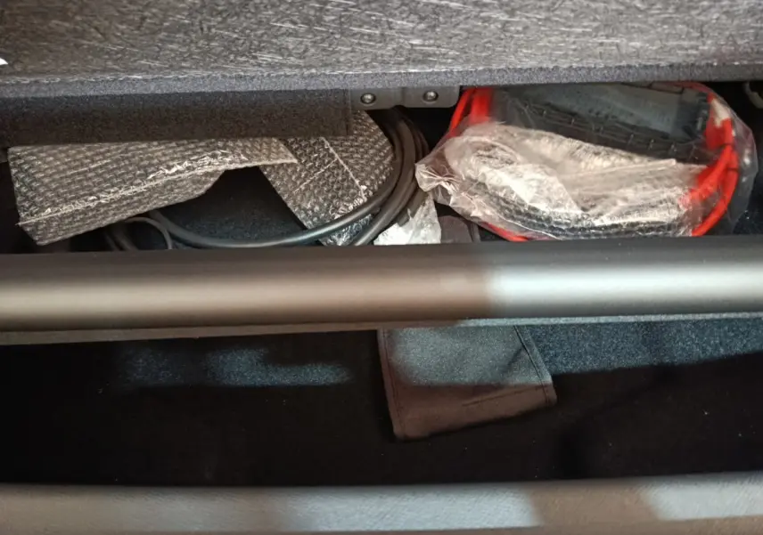 Vue intérieure du coffre du Peugeot 5008 gris clair, montrant câbles et accessoires de recharge rangés sous la tablette.